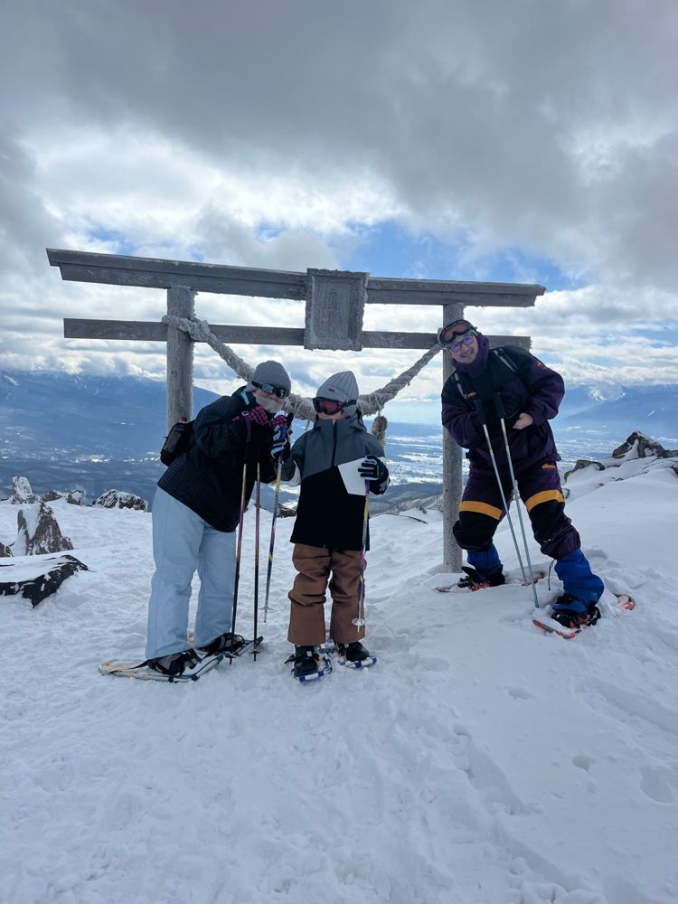 A family on snowshoes in front of a frosted wooden torii on the summit