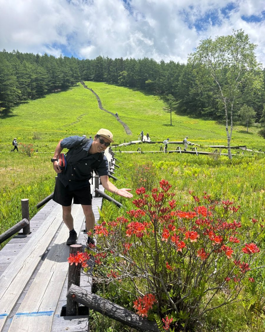 Toru "Reck" Fujita smiling beside red azaleas on a highland boardwalk