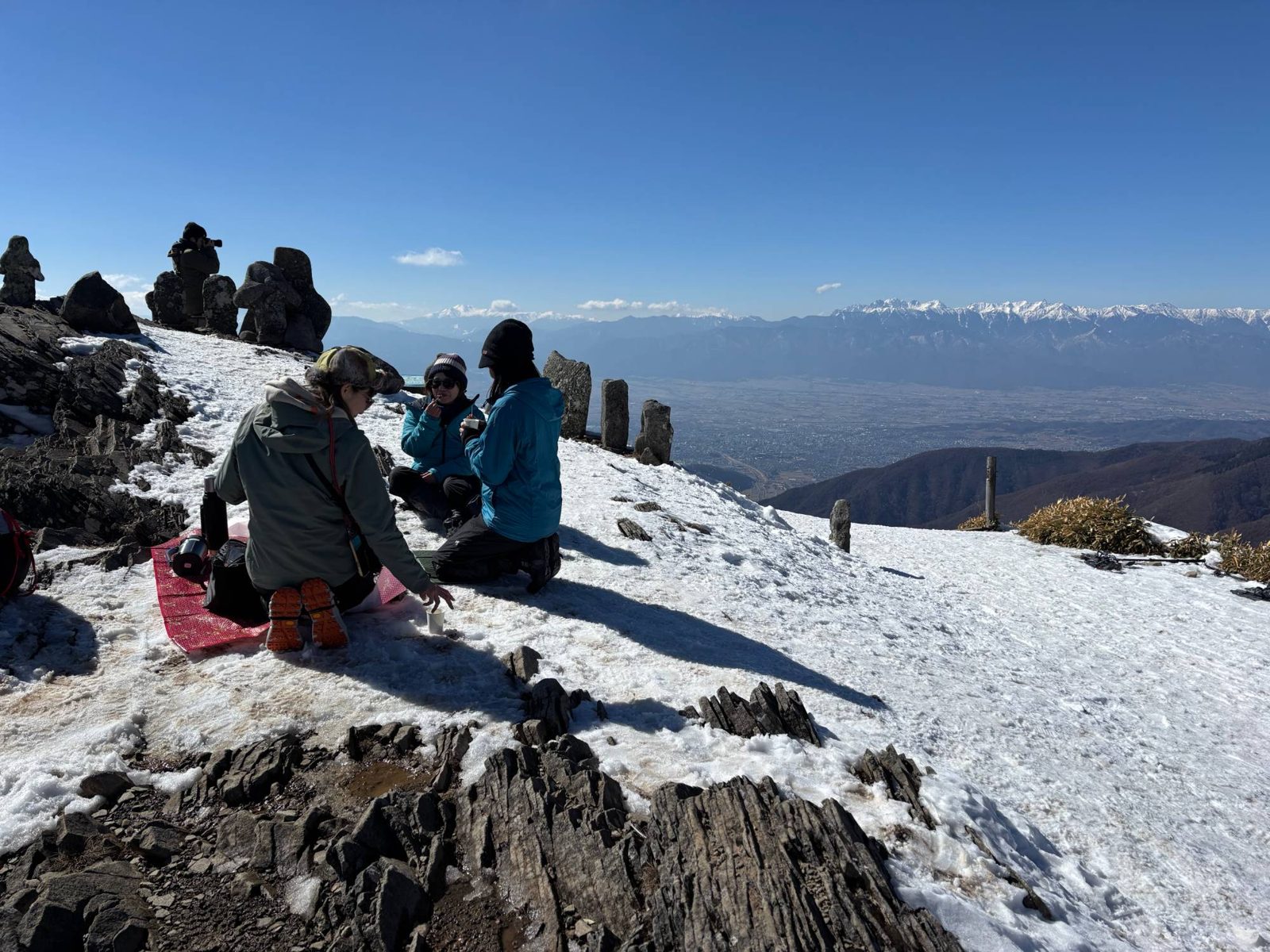 Guests taking a break on the snowy Utsukushigahara summit with the Northern Alps behind